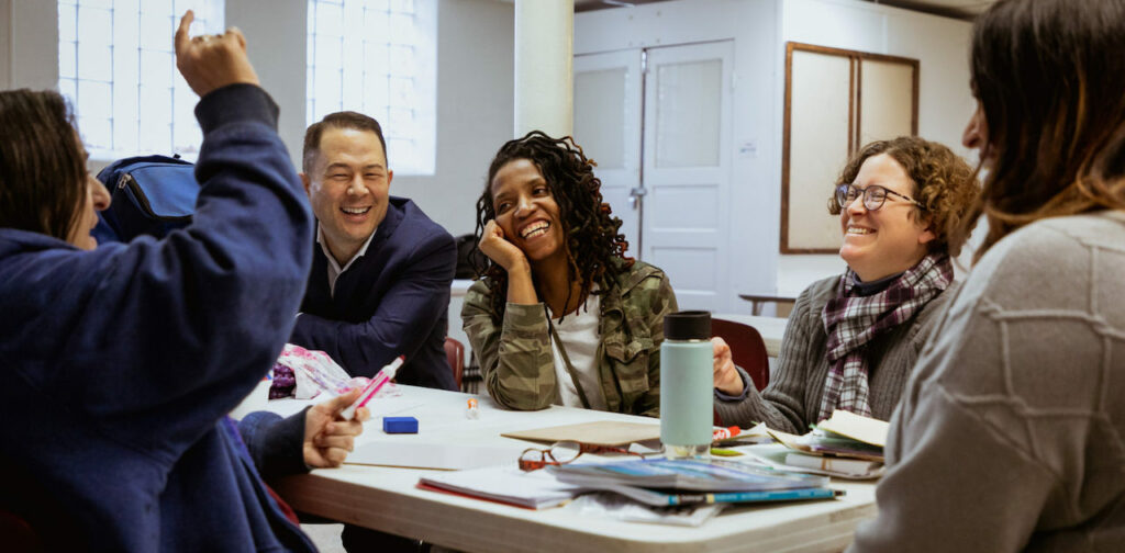 A group of students laugh around a table with a board member.