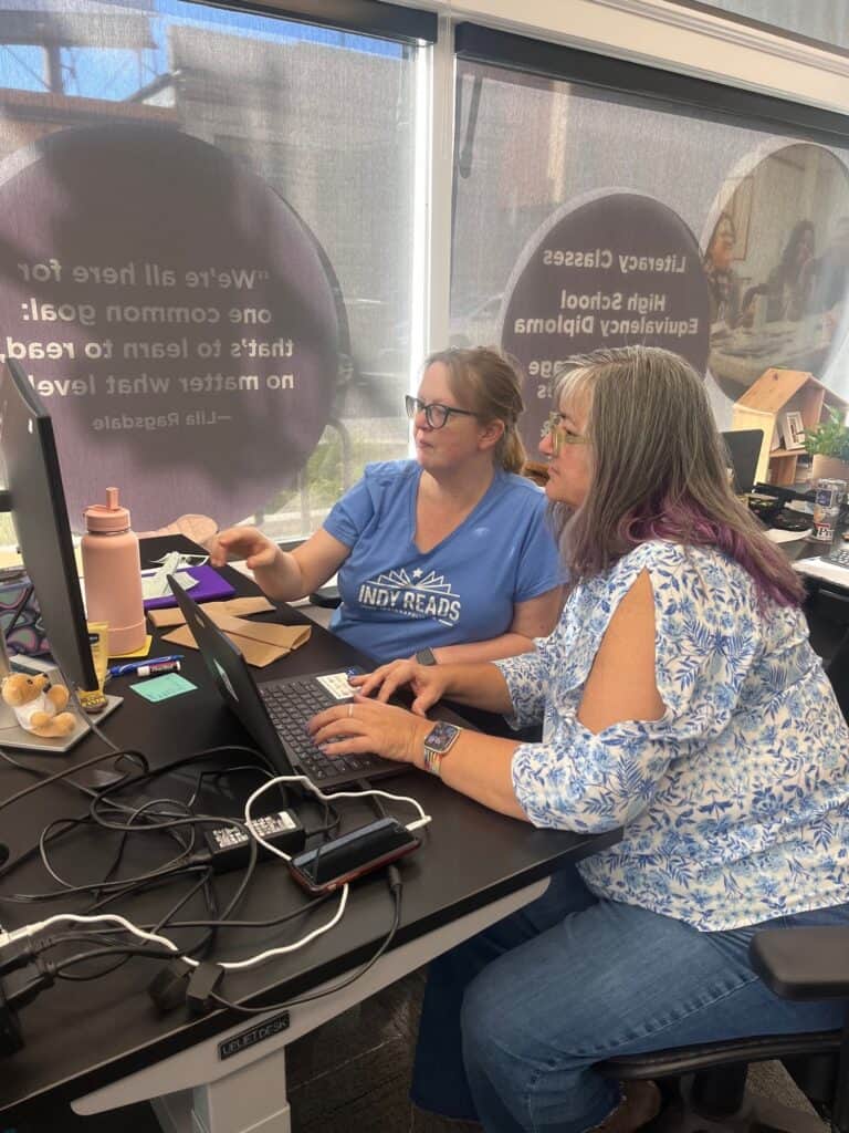 Two volunteers work together at a computer in the Indy Reads office